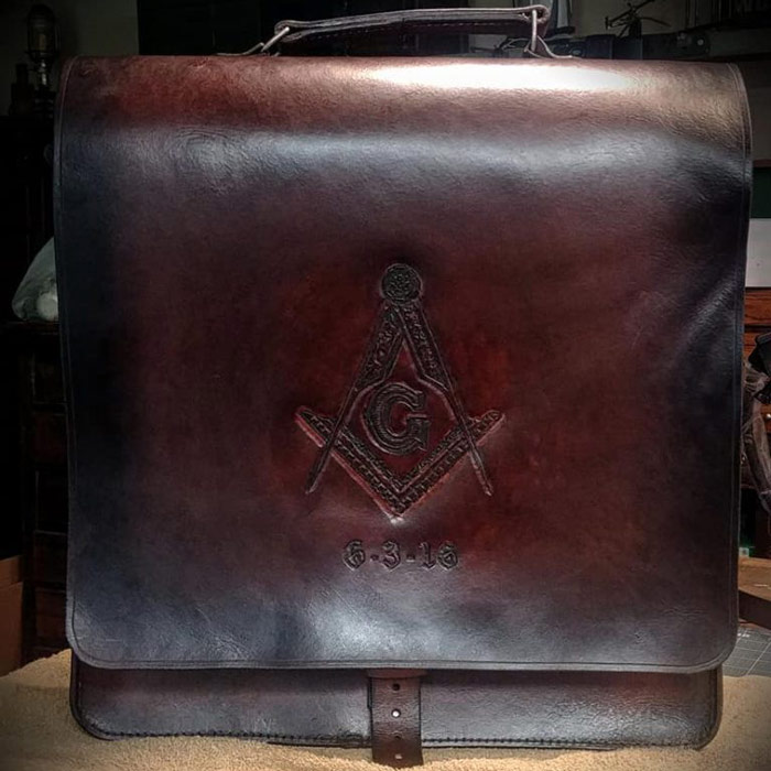 Dark brown leather messenger bag with mason symbol hand tooled on top flap.