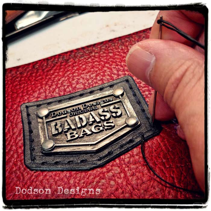 Don hand stitching on the Badass Bag metal logo on a red leather bag.