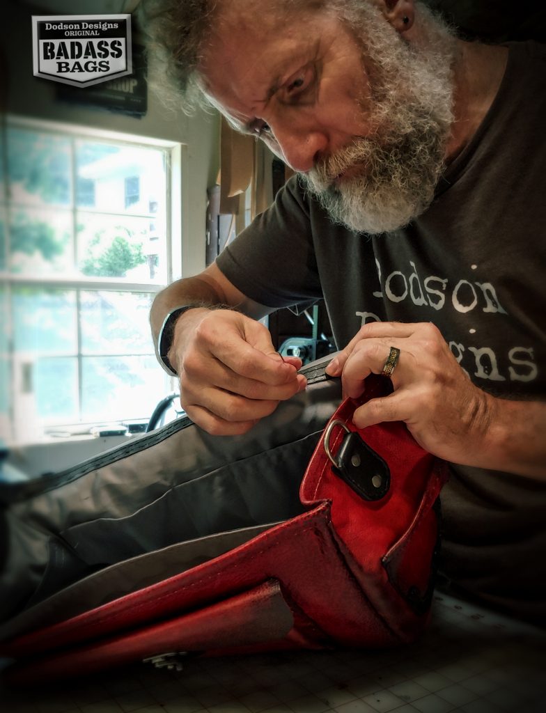 Don hand stitching a black fabric lining into a red leather badass bag.
