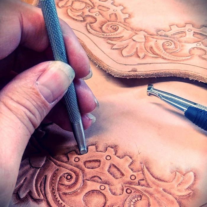 Close up of Donald Dodson's hand as he creates an embossed steampunk design in a leather bag.